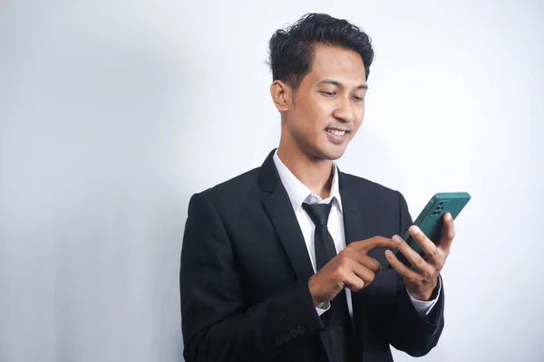 Portrait of a happy Asian young man wearing a suit while pointing at a mobile phone