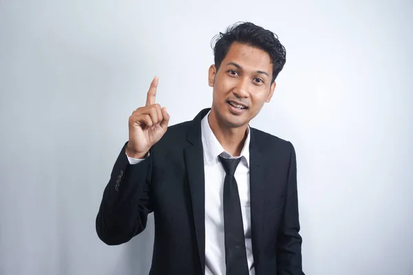 Attractive young asian man in suit pointing up with his finger isolated on gray background