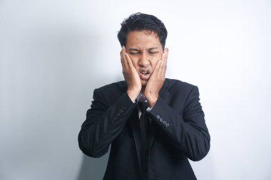 Diş ağrısı konsepti. Kapalı alanda, acı çeken genç bir erkeğin kötü diş ağrısından muzdarip yanağını tutarken, acı dolu bir ifadeyle kameraya bakarken.