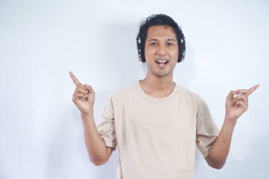 Asian man wearing headphones smiling amazed and surprised and pointing up with fingers and raised arms. isolated on white background