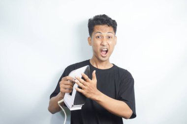 Siyah tişörtlü genç Asyalı adam komik bir ifadeyle kızgın demire dokunuyor ve şok, acı ve sıcağı ifade ediyor.