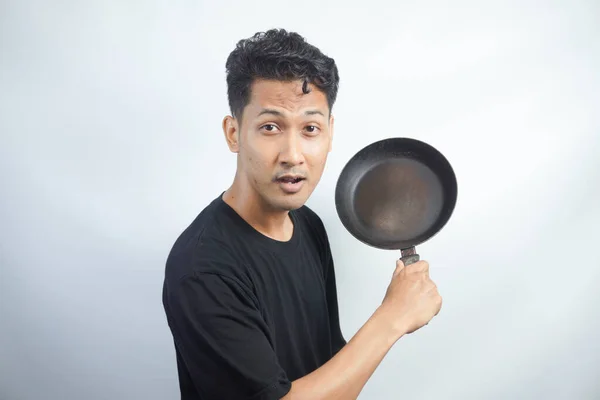 Young Asian man is angry and ready to strike with a frying pan. Indonesia Man wear black shirt Isolated grey background.