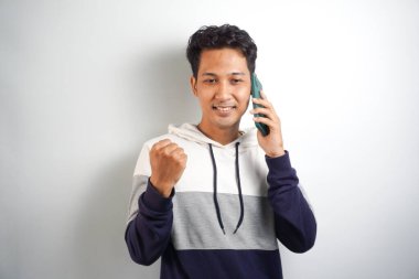 Excited happy young asian man winner feeling joy using smartphone winning lottery game, betting, getting cashback online gift in mobile app message holding cell phone isolated on white background.