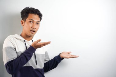 Yüzünde kocaman bir gülümseme olan sıradan bir kış kapüşonu giyen Asyalı yakışıklı adam kameraya el ve parmak ile bakıyor..