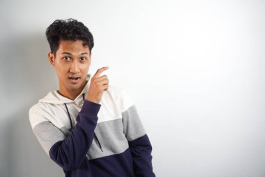 Yüzünde kocaman bir gülümseme olan sıradan bir kış kapüşonu giyen Asyalı yakışıklı adam kameraya el ve parmak ile bakıyor..