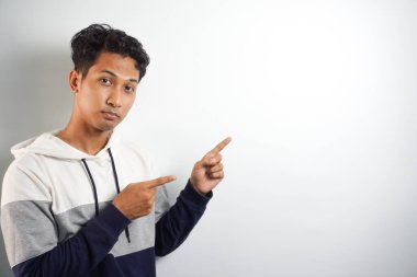 Yüzünde kocaman bir gülümseme olan sıradan bir kış kapüşonu giyen Asyalı yakışıklı adam kameraya el ve parmak ile bakıyor..