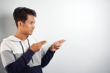 Yüzünde kocaman bir gülümseme olan sıradan bir kış kapüşonu giyen Asyalı yakışıklı adam kameraya el ve parmak ile bakıyor..