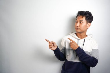 Yüzünde kocaman bir gülümseme olan sıradan bir kış kapüşonu giyen Asyalı yakışıklı adam kameraya el ve parmak ile bakıyor..