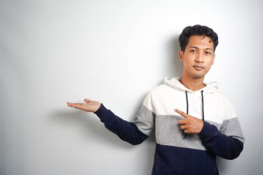 Yüzünde kocaman bir gülümseme olan sıradan bir kış kapüşonu giyen Asyalı yakışıklı adam kameraya el ve parmak ile bakıyor..