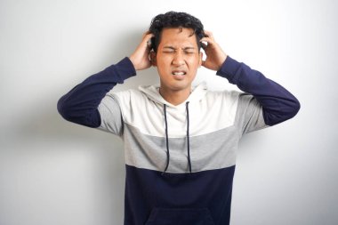 Gri arka planda izole edilmiş yakışıklı Asyalı adamın yatay fotoğrafı kafasının ne kadar acıdığını, acı çektiğini, perişan ve bitkin göründüğünü gösteriyor.