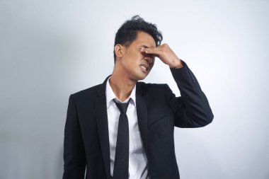 Yorgun, yorgun, takım elbiseli, göz ağrısı çeken Asyalı bir adam.