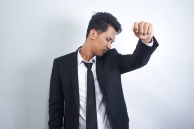 A man smells his underarm through his suit. Checking for signs of body odor from his armpit. His Antiperspirant is working. Isolated on a white background.