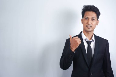 İş kıyafetleri giymiş yakışıklı Asyalı genç adam gülümsüyor ve kameraya bakıyor elleri ve parmakları yana bakıyor..