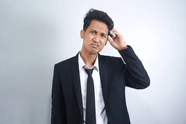 stock image Young handsome Asian man wearing suit standing over white background confuse and wonder about question. Uncertain with doubt, thinking with hand on head. Pensive concept.