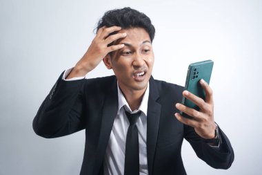 handsome young asian man wearing suit is angry and looking at cellphone