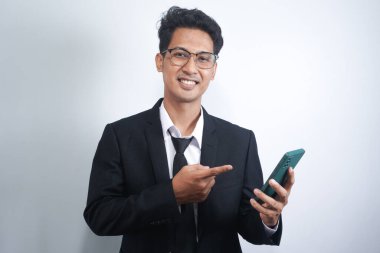 Portrait of a happy Asian young man wearing a suit while pointing at a mobile phone