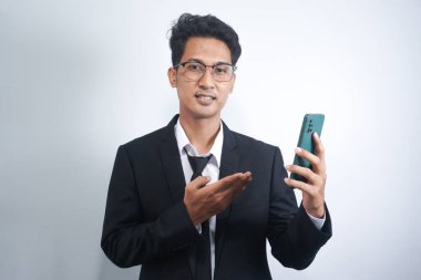 Portrait of a happy Asian young man wearing a suit while pointing at a mobile phone