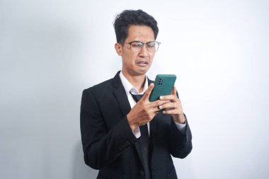 Asian guy wearing a suit looks sad reading online news from his cellphone. man shows disappointed gesture by wiping tears from his face
