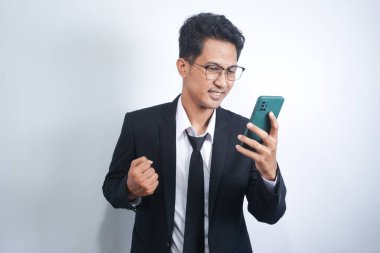 Excited happy young Asian man winner feeling joy using smartphone winning lottery game, betting, getting cashback online gift in mobile app message holding cell phone isolated on white background.