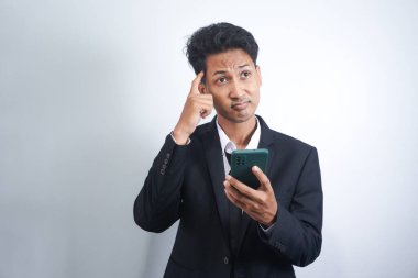 Yakışıklı genç yetişkin portresi, rüya gibi bakışlı, akıllı telefonu tutarken düşünen, beyaz arka planda izole edilmiş..