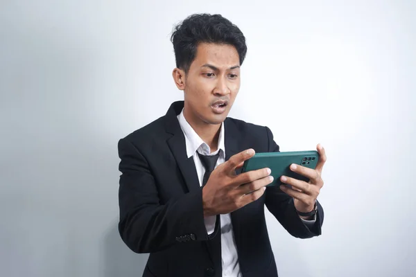 Angry Asian young man get mad on the smartphone when play game at work. Indonesian man wearing suit.