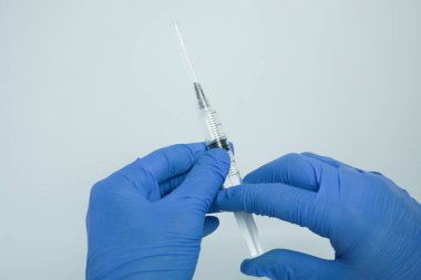 Beyaz arka planda izole edilmiş enjeksiyon için plastik şırınga tutan mavi eldivenli bir erkek. Sağlık, tedavi kavramı
