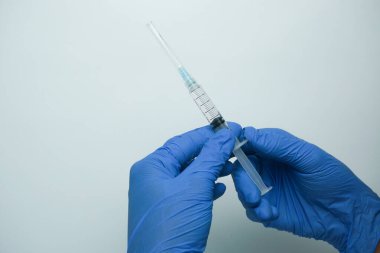 Beyaz arka planda izole edilmiş enjeksiyon için plastik şırınga tutan mavi eldivenli bir erkek. Sağlık, tedavi kavramı
