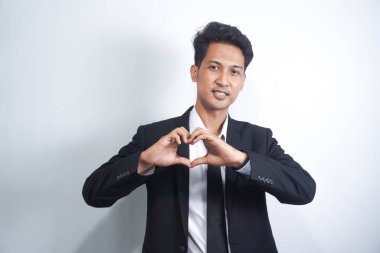 Gülümseyen genç bir adamın portresi elleri göğsünde, kalp şeklinde, sempatisini ifade ediyor. İyi kalpli, dost canlısı, takım elbiseli iyi bir adam.