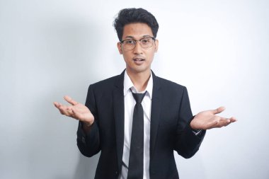 Bilmiyorum, kimin umrunda. Takım elbiseli, omuzlarını silkeleyen kafası karışık Asyalı bir adamın portresi. Beyaz arka planda izole edilmiş kapalı stüdyo çekimi