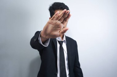 Yakışıklı Asyalı takım elbiseli genç ciddi ciddi dur hareketi yapıyor. El hareketi, yüzünü gizleme, dur işareti.