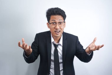 Bilmiyorum, kimin umrunda. Takım elbiseli, omuzlarını silkeleyen kafası karışık Asyalı bir adamın portresi. Beyaz arka planda izole edilmiş kapalı stüdyo çekimi