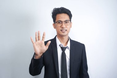 Genç yakışıklı Asyalı adam izole edilmiş arka planda duruyor ve beş numaralı parmaklarıyla işaret ederken kendinden emin ve mutlu bir şekilde gülümsüyor..