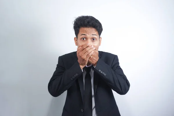 stock image The Asian young man wearing suit, in shock, covers his mouth with his hands, thinking, No, this is impossible.