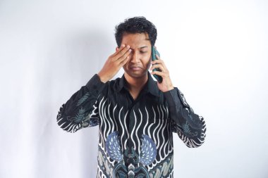 Batik tişört giyen Asyalı adam telefonla kötü haber alıyor.