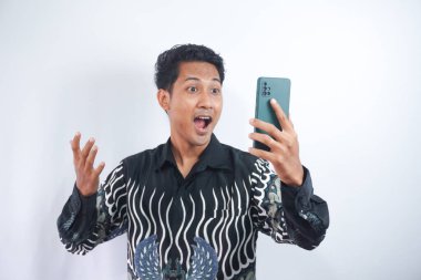 Beyaz arka planda izole edilmiş, bağıran ve cep telefonuna bakan pozitif heyecanlı adamın fotoğrafı.