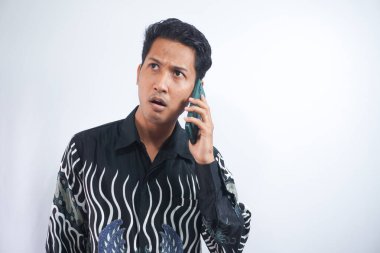 Batik tişört giyen Asyalı genç adam telefonda kafası karışmış.