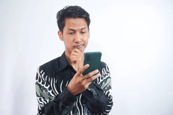 Giovane Uomo Premuroso Indossa Batik Camicia Guardando Telefono Cellulare Pensando — Foto Stock
