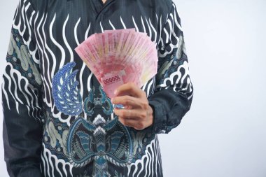 Batik tişörtlü adam rupiah banknotları tutuyor ve para veriyor, çok para, izole edilmiş. Finans kavramı