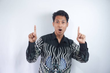 Asyalı adam Batik gömleği giyer, elini kaldırır, reklamını yapar, parmaklarını havaya kaldırır, sırıtır, davet eder, kullanım linki dener, ürün dener, yön verir, beyaz arka planda durur.