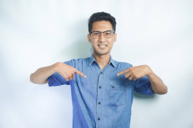 Mavi gömlekli Asyalı genç adam kendini işaret ediyor. Mavi gömlekli adam kendi reklamını yapıyor, başarısıyla övünüyor, beyaz arka planda duruyor.