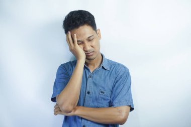 Beyaz arka planda mavi gömlekli yakışıklı genç adam. Esniyor ve yorgun bir şekilde uyuyor.