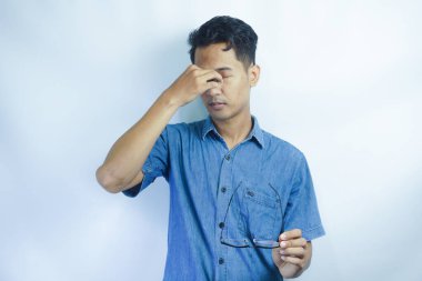 Mavi gömlek giyen genç yakışıklı adam yorgunluk ve baş ağrısı için gözlerini ovuşturuyor, uykulu ve yorgun ifade. görme sorunu