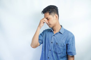 Mavi gömlek giyen genç yakışıklı adam yorgunluk ve baş ağrısı için gözlerini ovuşturuyor, uykulu ve yorgun ifade. görme sorunu