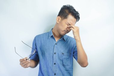 Mavi gömlek giyen genç yakışıklı adam yorgunluk ve baş ağrısı için gözlerini ovuşturuyor, uykulu ve yorgun ifade. görme sorunu