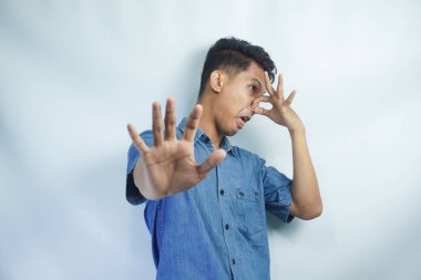 Stop unpleasant smell. Portrait of young man in denim casual shirt displeased by stink, grimacing in disgust and pinching his nose, making no gesture. indoor studio shot isolated on yellow background clipart