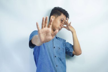 Stop unpleasant smell. Portrait of young man in denim casual shirt displeased by stink, grimacing in disgust and pinching his nose, making no gesture. indoor studio shot isolated on white background