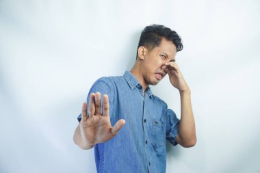 Kötü kokmayı bırak. Kokudan rahatsız olan, tiksinti içinde yüzünü buruşturan, jest yapmayan kot gömlekli genç bir adamın portresi. Sarı arka planda izole edilmiş kapalı stüdyo çekimi