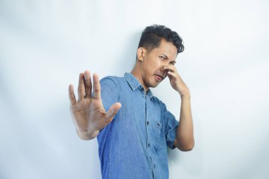 Kötü kokmayı bırak. Kokudan rahatsız olan, tiksinti içinde yüzünü buruşturan, jest yapmayan kot gömlekli genç bir adamın portresi. Sarı arka planda izole edilmiş kapalı stüdyo çekimi