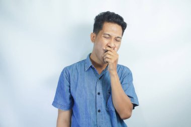 Genç yakışıklı adam izole edilmiş arka planda esniyor ve elleriyle ağzını kapatıyor.