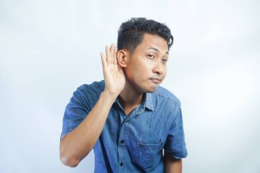 Genç Asyalı çılgın adam ciddi ve meraklı görünüyor, dinliyor, gizli bir konuşma ya da dedikodu duymaya çalışıyor, düz renkli duvara kulak misafiri oluyor.